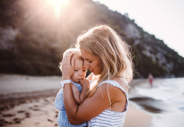 Young mother with a toddler girl on beach on summer holiday at sunset. - Fotoğraf, Görsel