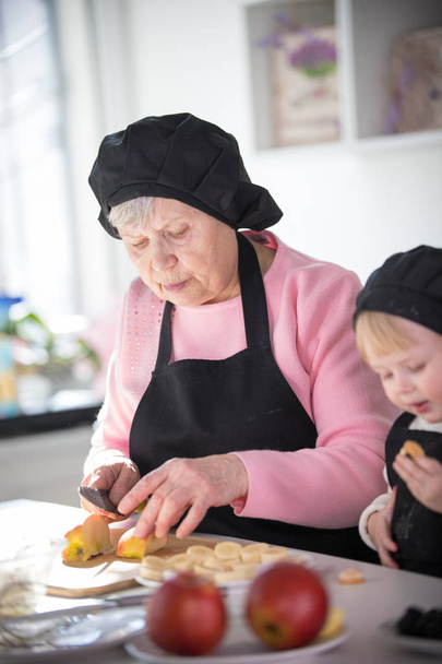 Stara kobieta cięcie jabłko z małą dziewczynką w kuchni - Zdjęcie, obraz
