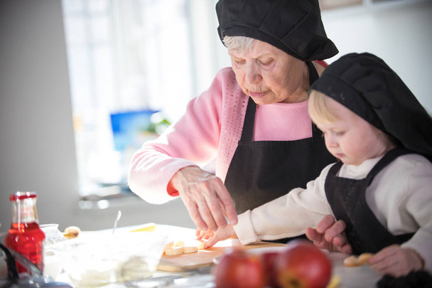 Una anciana con una niña en la cocina. Una niña toma un pedazo de plátano
 - Foto, Imagen
