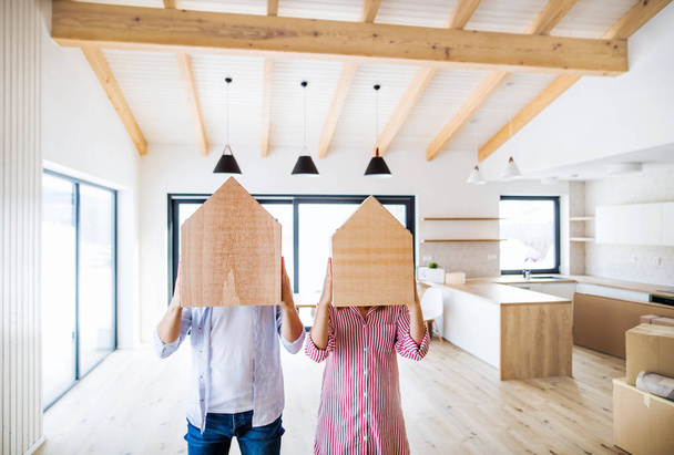 A young couple covering faces with wooden house. A moving in new home. - Photo, image