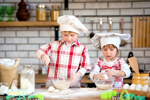 I bambini un ragazzo e una ragazza preparano deliziosi pan di zenzero e biscotti in cucina da farina e uova
 - Foto, immagini