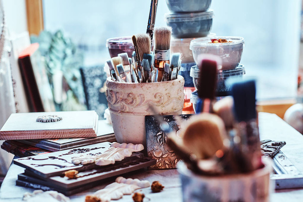 A lot of different brushes on artists table in jars. There are artisticks mess on the table - Fotografie, Obrázek