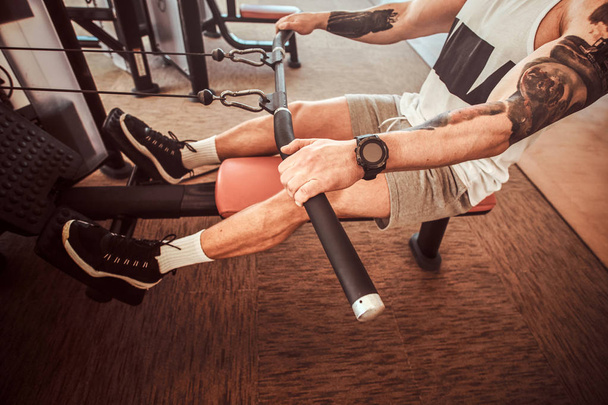 Hombre musculoso joven con tatuajes está haciendo ejercicios en la máquina de remo
 - Foto, Imagen