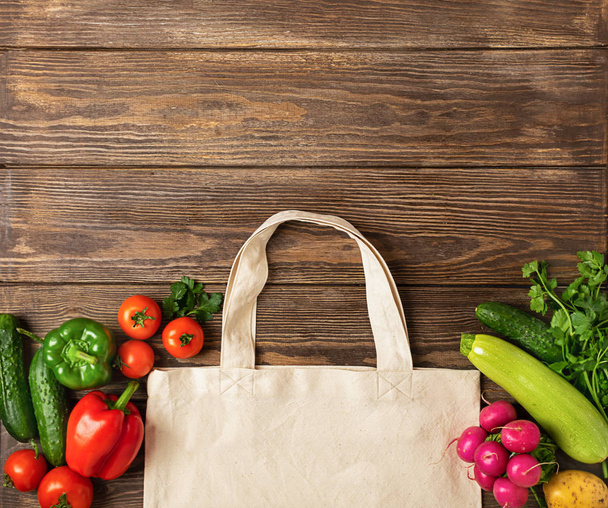 Baumwolle Einkaufstasche und frisches rustikales Gemüse auf einem hölzernen Hintergrund. Öko-Konzept. Kopierraum. flache Aufteilung. - Foto, Bild
