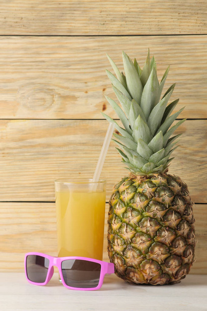 Ripe pineapple fruit and pineapple juice and sunglasses on a natural wooden background. summer. - Фото, зображення