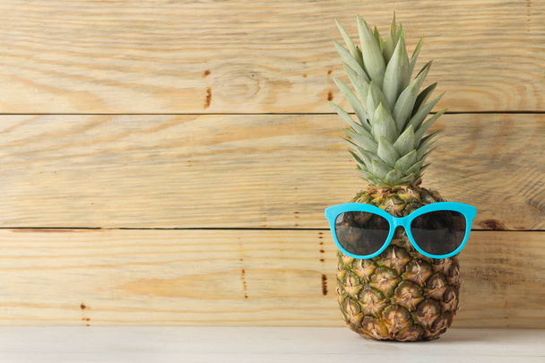 Piña de fruta madura en gafas de sol sobre un fondo de madera natural. Verano. espacio para texto
 - Foto, imagen