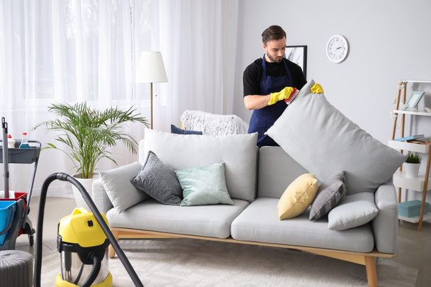 männlicher Hausmeister putzt Sofa im Zimmer - Foto, Bild
