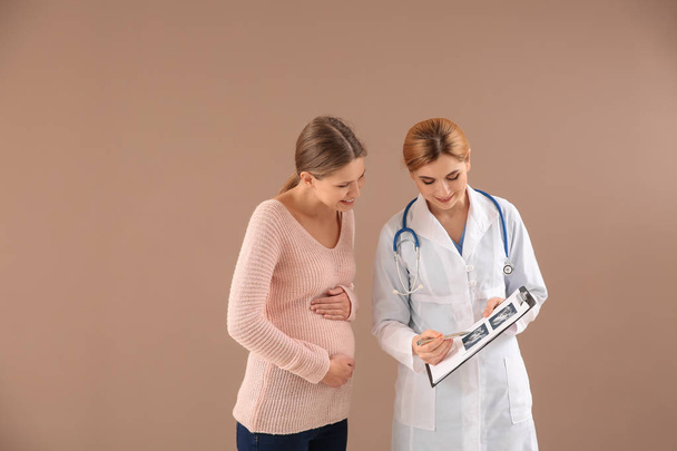 Gynekolog s mladou těhotnou ženou na barevném pozadí - Fotografie, Obrázek