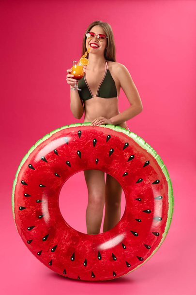 Krásná mladá žena s nafukuným prstenem a koktejlem na pozadí barev - Fotografie, Obrázek