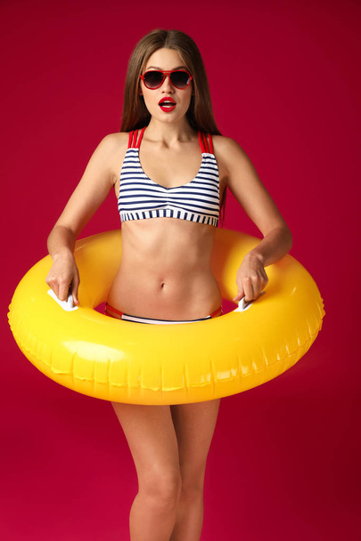 Surprised young woman with inflatable ring on color background - Foto, Imagem