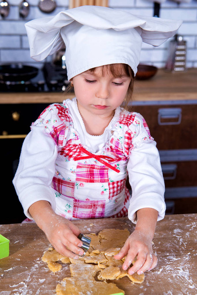 Keittiömestarin hattuinen tyttö tekee piparkakkuja keittiössä, tekee kakkuja keksipurkeista.
 - Valokuva, kuva