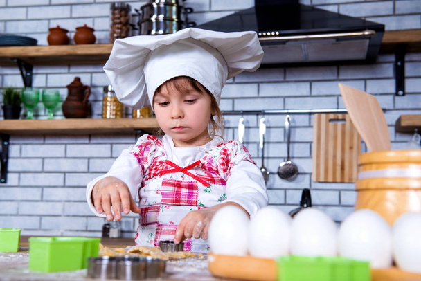 A girl in a chef's hat is cooking gingerbread in the kitchen, making cakes from cookies tins - Φωτογραφία, εικόνα