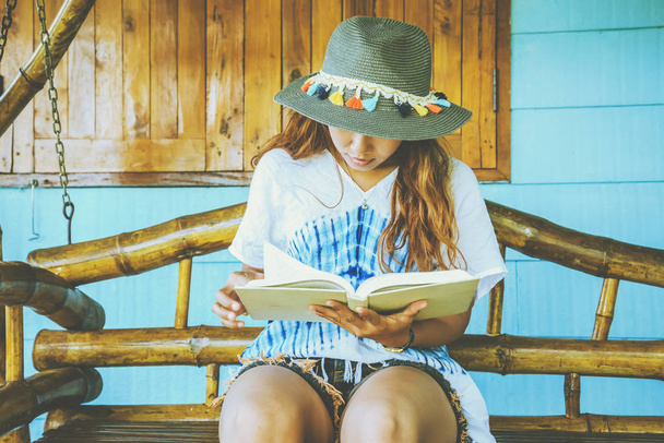 As mulheres asiáticas relaxam nas férias. sente-se leia um livro em um balanço de madeira. Alpendre da frente. Na Tailândia
 - Foto, Imagem