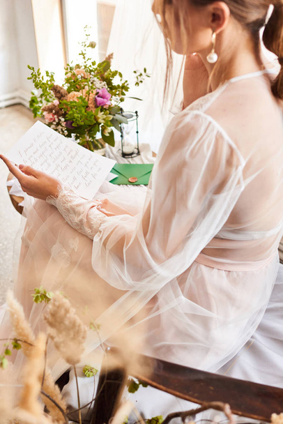 Trouwdag. De bruid zit in de buurt van het raam en leest de brief aan de bruidegom. Huwelijksgeloften. Preparaten. Ochtend van de bruid - Foto, afbeelding