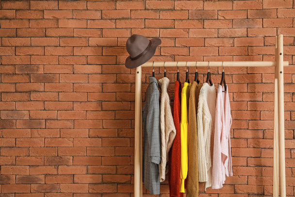 Stojak ze stylowymi ubraniami na tle cegły - Zdjęcie, obraz