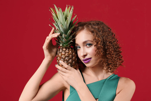 Mooie jonge vrouw in badpak en met smakelijke ananas op kleur achtergrond - Foto, afbeelding