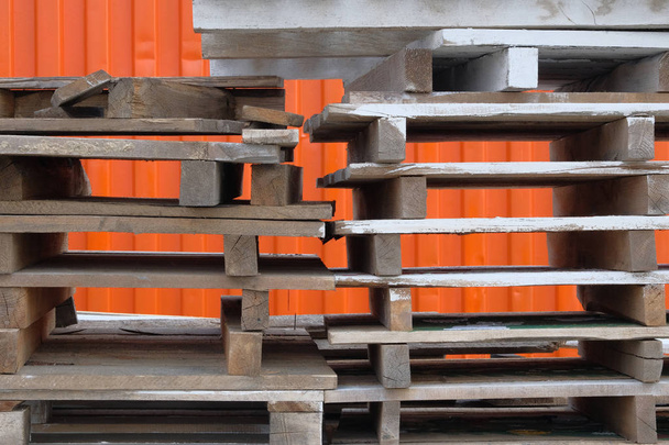 Montones de paletas de madera en bruto de colores en el almacén en el patio industrial. Paletas sobre fondo naranja. Concepto de carga y envío
. - Foto, imagen