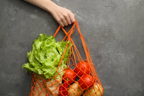 Female hand with fresh vegetables and mesh shopping bag on grunge background. Zero waste concept - Foto, Imagen