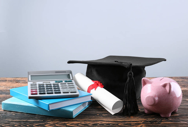 Mortar board, books, calculator, diploma and piggy bank on table. Fee-paying education concept - Photo, Image