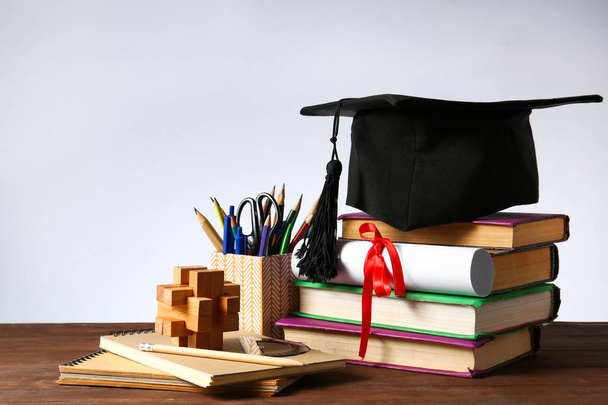 Placa de argamassa, diploma, artigos de papelaria e livros na mesa. Conceito de graduação do ensino médio
 - Foto, Imagem