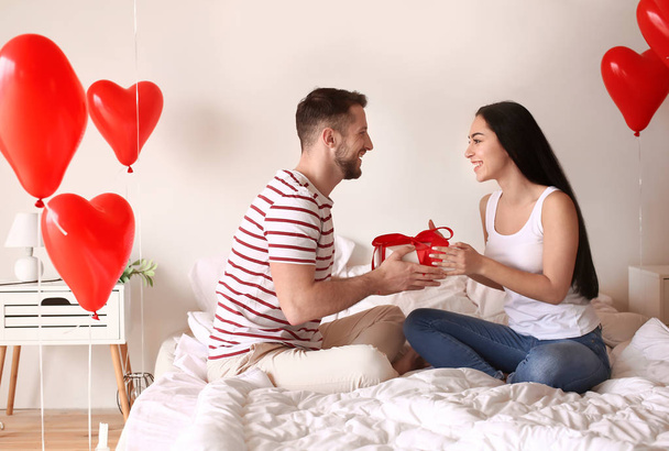 Happy young couple with gift at home on Valentine 's Day
 - Фото, изображение