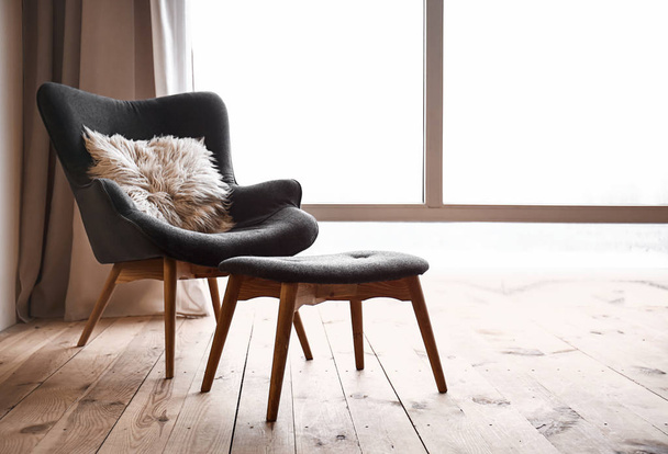 Удобное кресло и подставка для ног возле окна в квартире
 - Фото, изображение