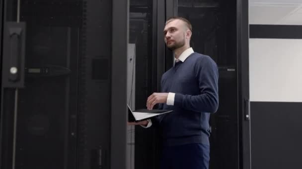 Administrator walking in server room and typing at laptop - Footage, Video