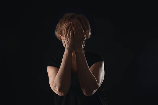 Itkevä kypsä nainen tummalla taustalla
 - Valokuva, kuva