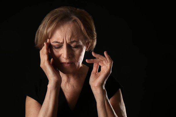 Красивая зрелая женщина страдает от головной боли на темном фоне
 - Фото, изображение