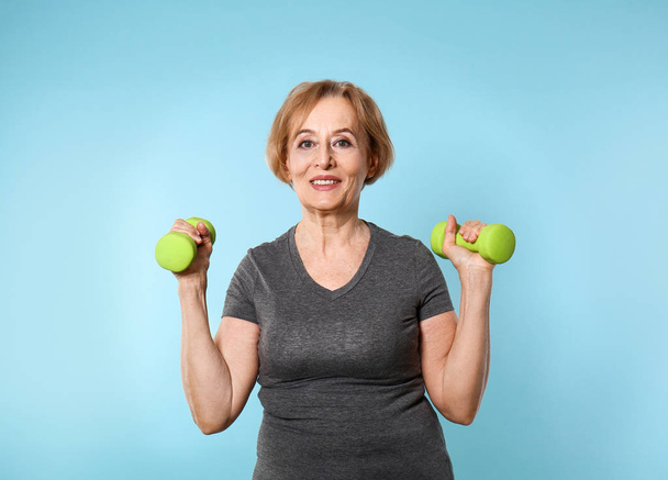 Beautiful mature woman with dumbbells on color background - Fotografie, Obrázek