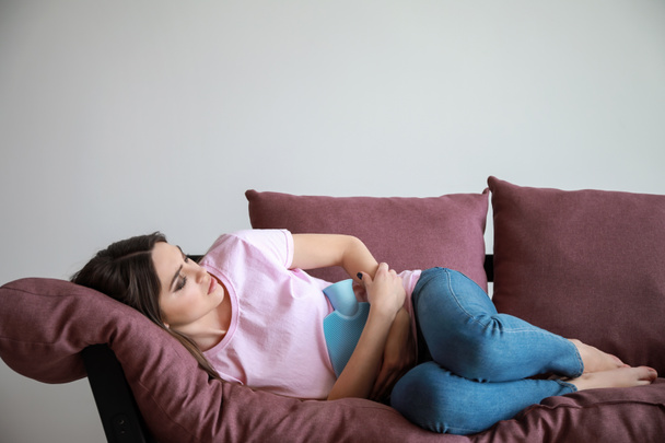 Jeune femme souffrant de douleurs abdominales tout en étant couché sur le canapé sur fond blanc
 - Photo, image