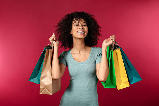 Happy African-American woman with shopping bags on color background - Φωτογραφία, εικόνα