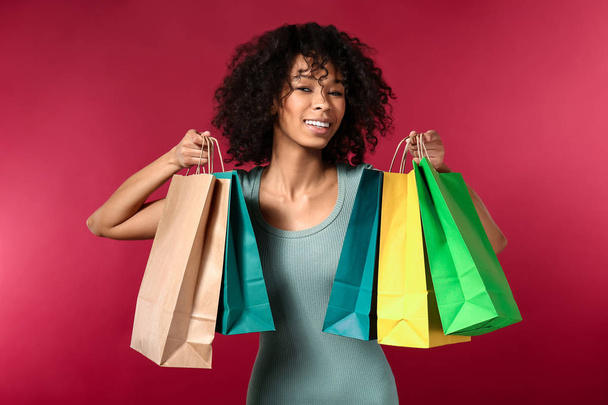 Χαρούμενη αφροαμερικάνικη γυναίκα με σακούλες για ψώνια στο χρώμα φόντου - Φωτογραφία, εικόνα