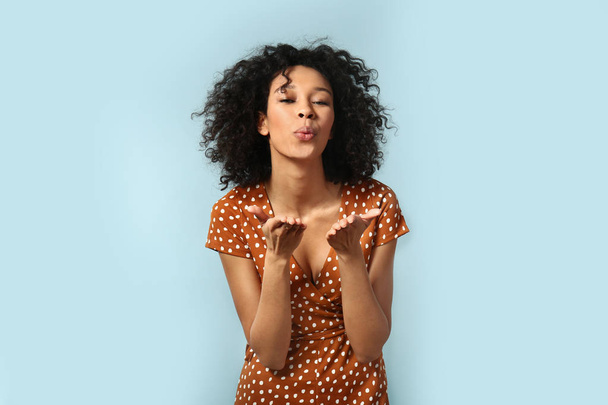 Young African-American woman blowing kiss on color background - Fotografie, Obrázek