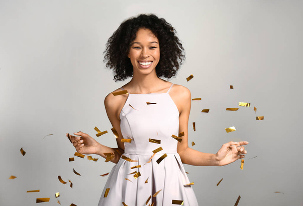 Happy African-American woman with falling confetti on grey background - Photo, Image