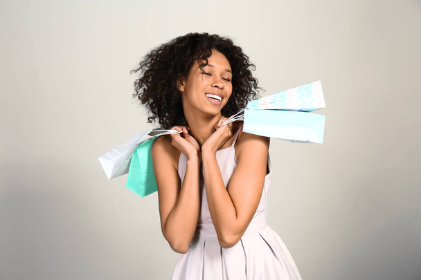 Happy African-American woman with shopping bags on grey background - Photo, Image
