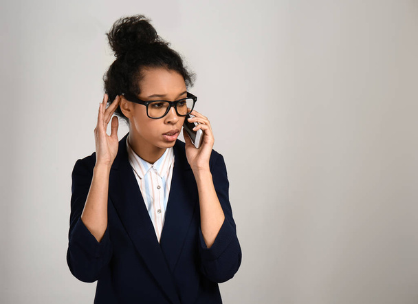 Młoda Afroamerykanka rozmawia przez telefon komórkowy na szarym tle - Zdjęcie, obraz