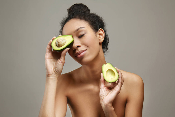 Молодая афроамериканка со здоровым авокадо на сером фоне
 - Фото, изображение