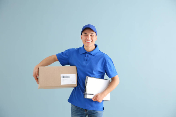 Delivery man with box and clipboard on color background - Photo, Image