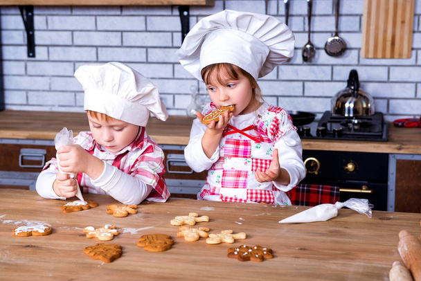 Children a girl and a boy in a cooking chef's hat decorate ready-made baked gingerbread with sweet icing and cream - Фото, изображение