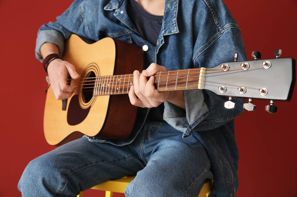 Przystojny młody człowiek gra na gitarze na kolorowym tle - Zdjęcie, obraz