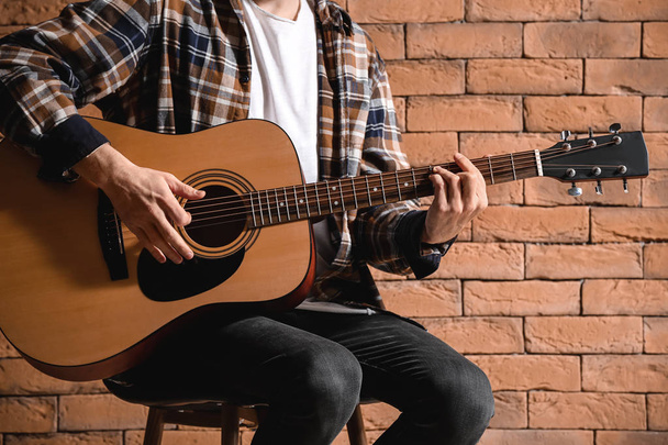 Handsome young man playing guitar against brick wall - 写真・画像