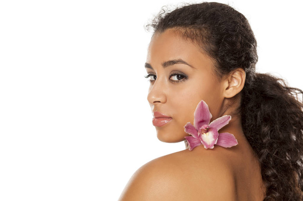 portrait of young beautiful dark-skinned woman with orchid on a white background - Photo, Image