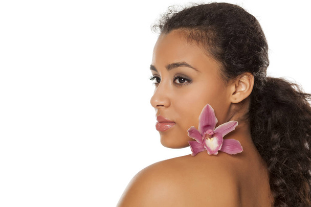 portrait of young beautiful dark-skinned woman with orchid on a white background - Photo, Image