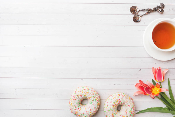 Cup of tea and donuts, flowers tulips on white table with copy space. Flat lay, top view. - Foto, imagen