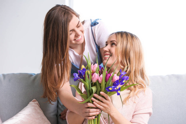 Daughter greeting her mother with flowers at home - Foto, Imagem