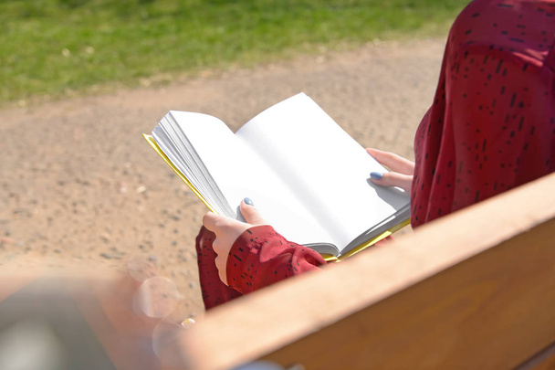 Beautiful young woman reading book on bench in park, closeup - 写真・画像