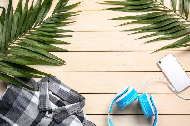 Shirt, headphones, tropical leaves and phone on wooden background - Photo, Image