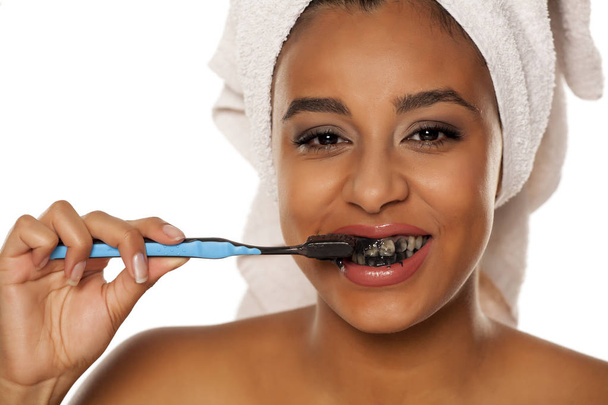 beyaz bir arka plan üzerinde siyah diş macunu ile dişlerini fırçalayan mutlu bir genç koyu tenli kadının portresi - Fotoğraf, Görsel