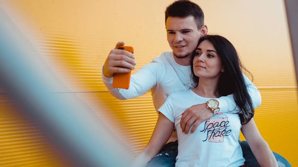 junges schönes Paar macht Selfie auf Smartphone vor gelbem Hintergrund - Foto, Bild